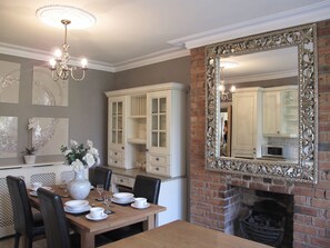 A dining area with a wooden table set for four, surrounded by chairs. There is a white cabinet with glass doors and a large ornate mirror above the fireplace. - Harrogate Boutique Apartments (Harrogate)