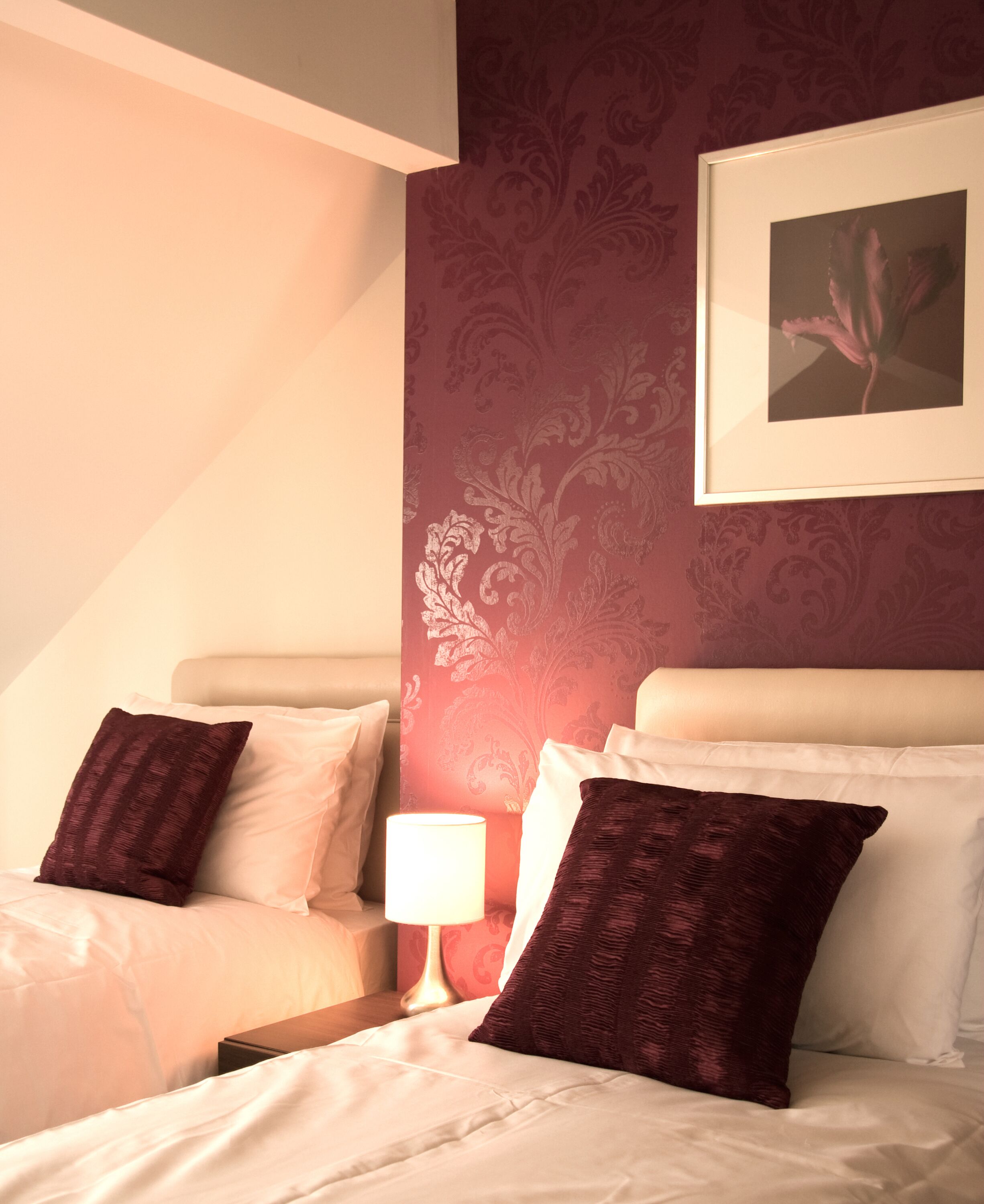 Ein Hotelzimmer mit einem Bett, zwei Kissen, einem Nachttisch, einer Lampe und einem gerahmten Bild an der Wand.