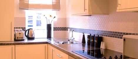 A modern kitchen with white cabinets, a granite countertop, a window with blinds, and a tiled backsplash.