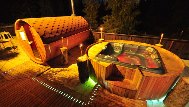A hot tub and a sauna on a wooden deck with string lights. - Hotel Rifugio Sores (Predaia)