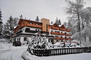 A multi-story hotel with a wooden facade and balconies, surrounded by snow-covered trees.