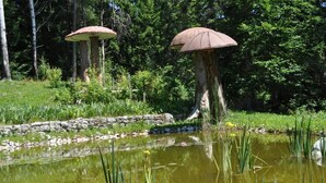 A pond with two mushroom-shaped structures, surrounded by greenery and trees. - Hotel Rifugio Sores (Predaia)