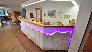A reception desk with a wooden finish and purple LED lighting. - Hotel Rifugio Sores (Predaia)