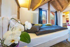 A bedroom with a bed, white orchid flowers, a window with blue curtains, and a wooden ceiling.