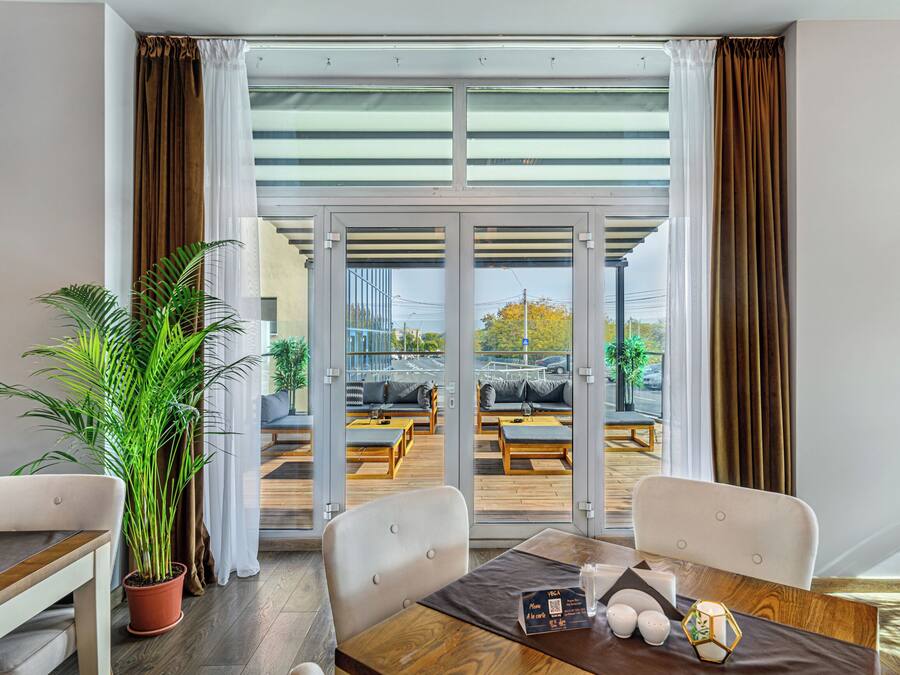 A modern hotel room with a dining area, a potted plant, and a view of the outdoor seating area.