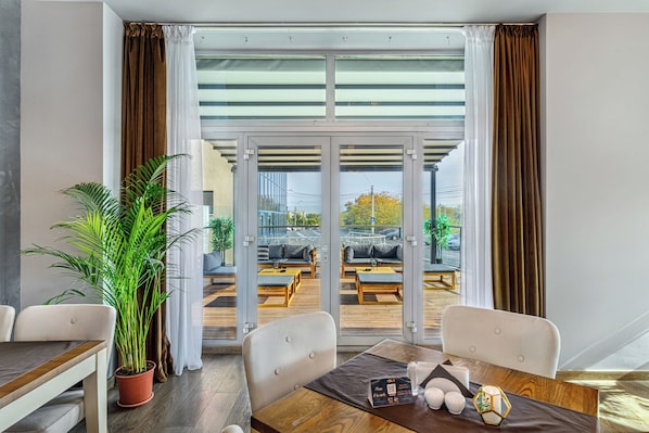 A modern hotel room with a dining area, a potted plant, and a view of the outdoor seating area. - Vega Hotel (Galati)