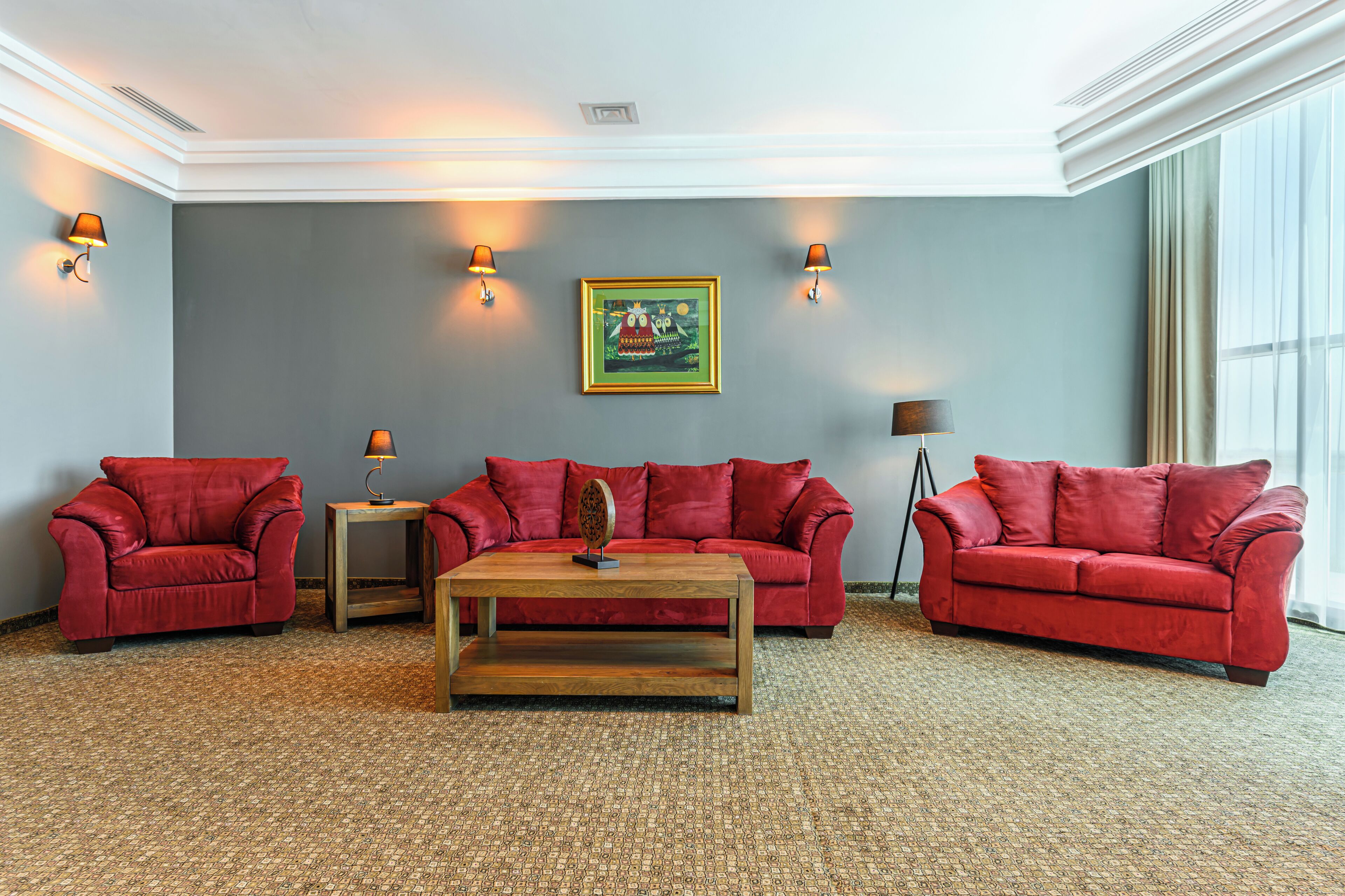 A room with three red sofas, a wooden coffee table, and two wall-mounted lamps.