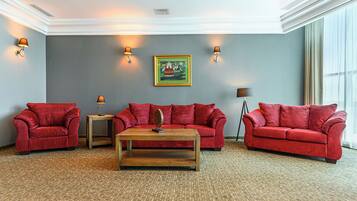 A room with three red sofas, a wooden coffee table, and two wall-mounted lamps.