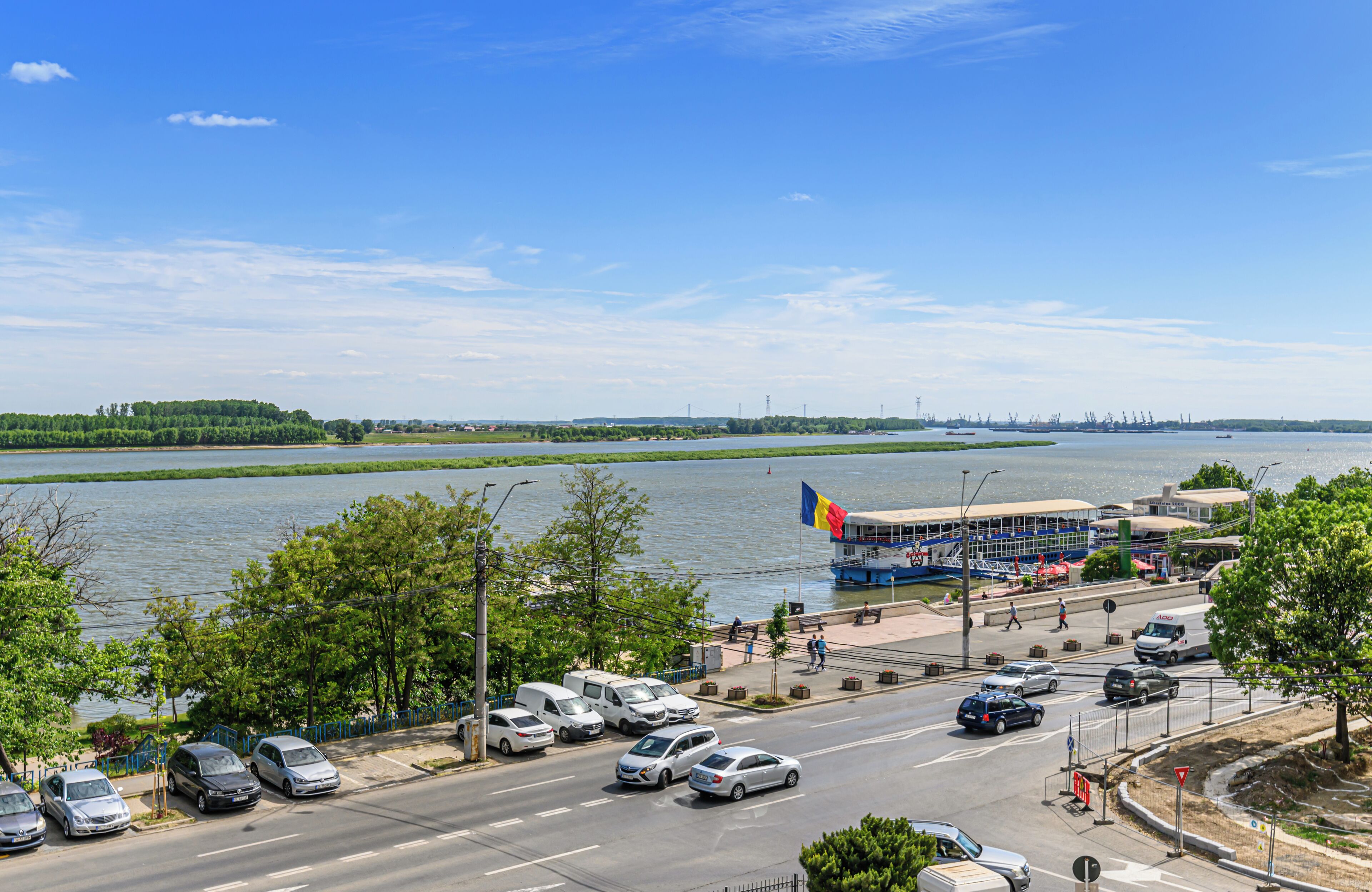 A waterfront view with a bus terminal, parked cars, and a river.