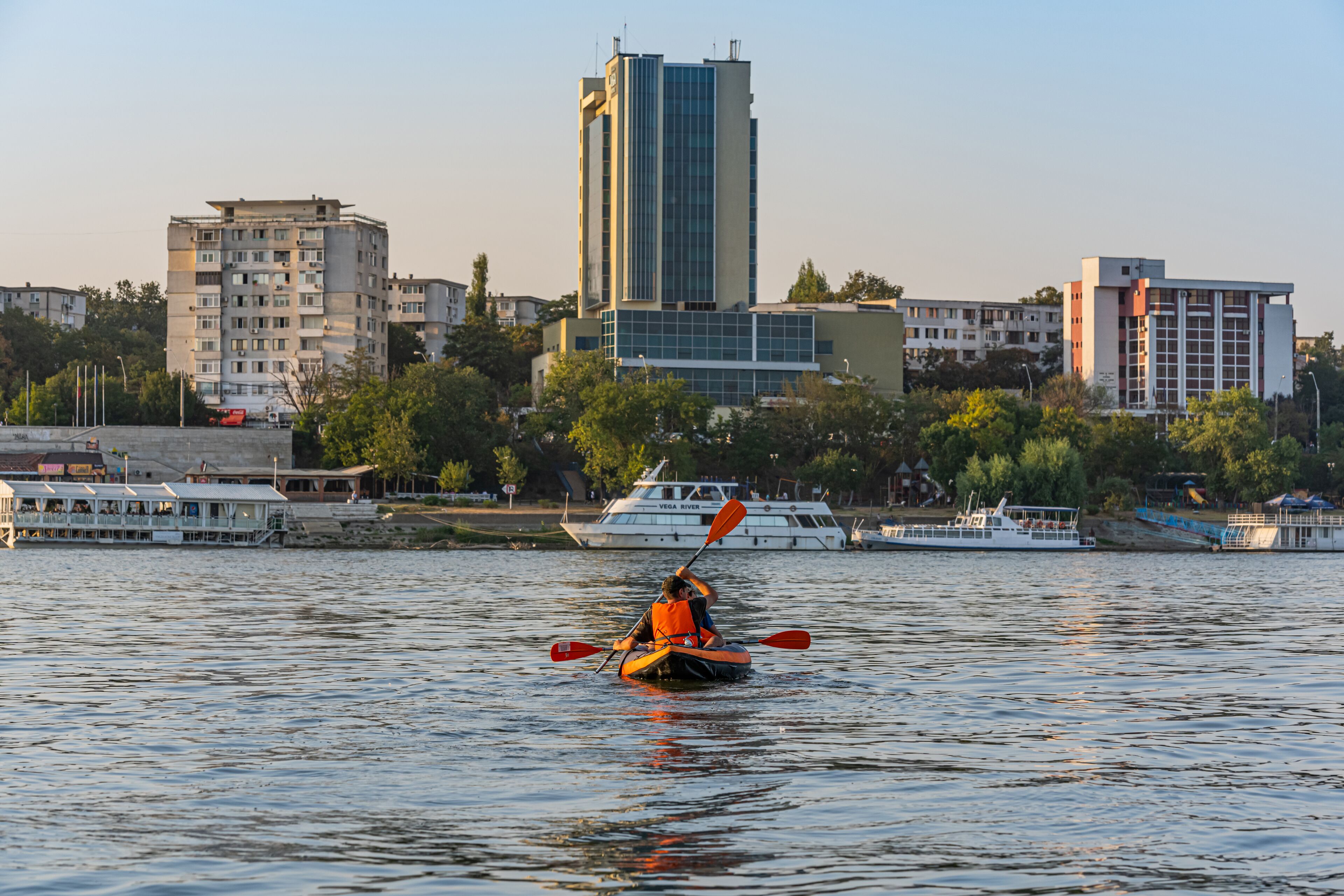 Un kayakista en un río, con un paisaje urbano al fondo.