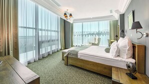 Une chambre d’hôtel avec un grand lit, une table de chevet en bois, un bureau et une vue sur la ville grâce à de grandes fenêtres.
