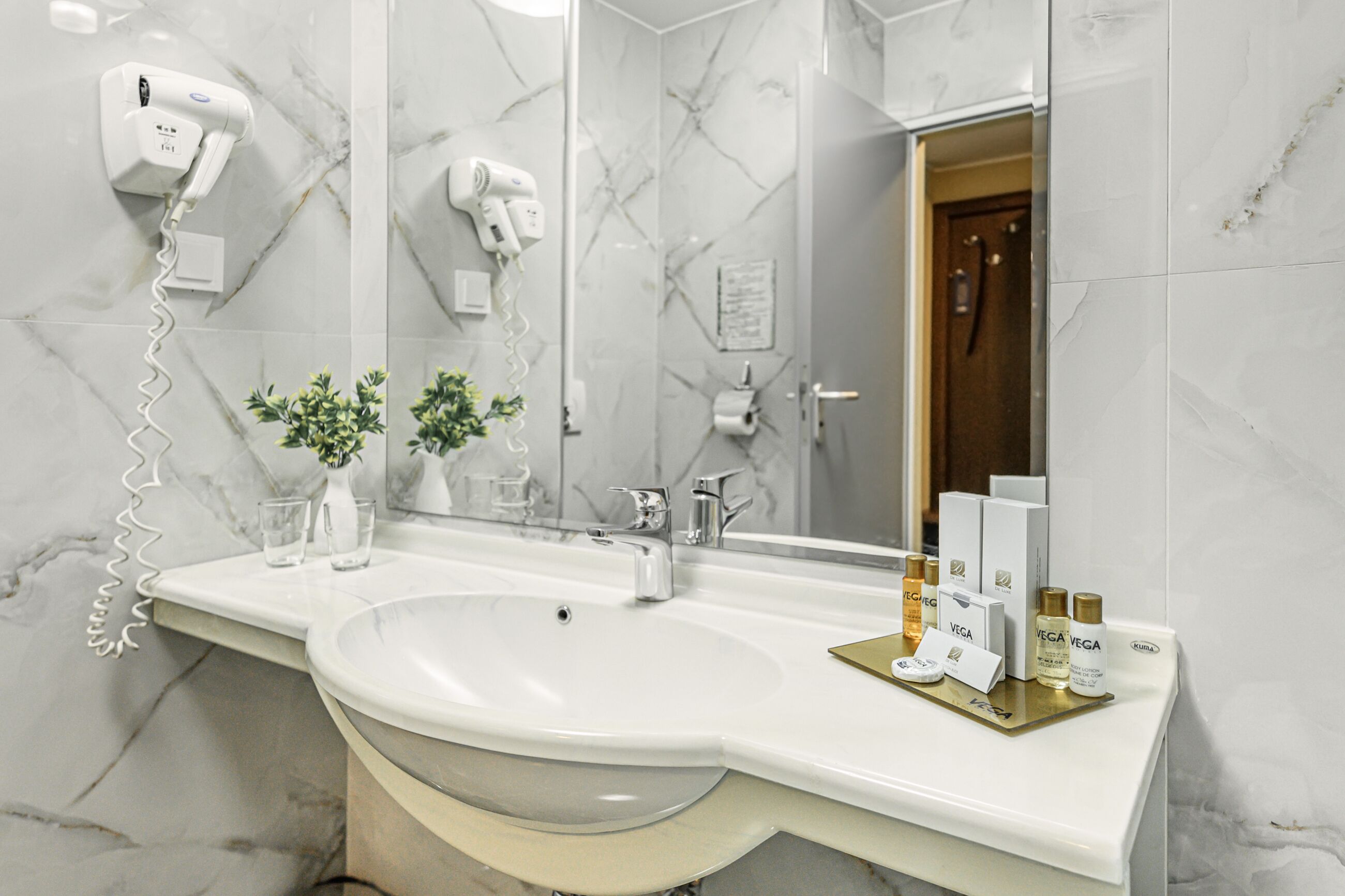 A bathroom with a large sink, a hairdryer, and toiletries on the counter.