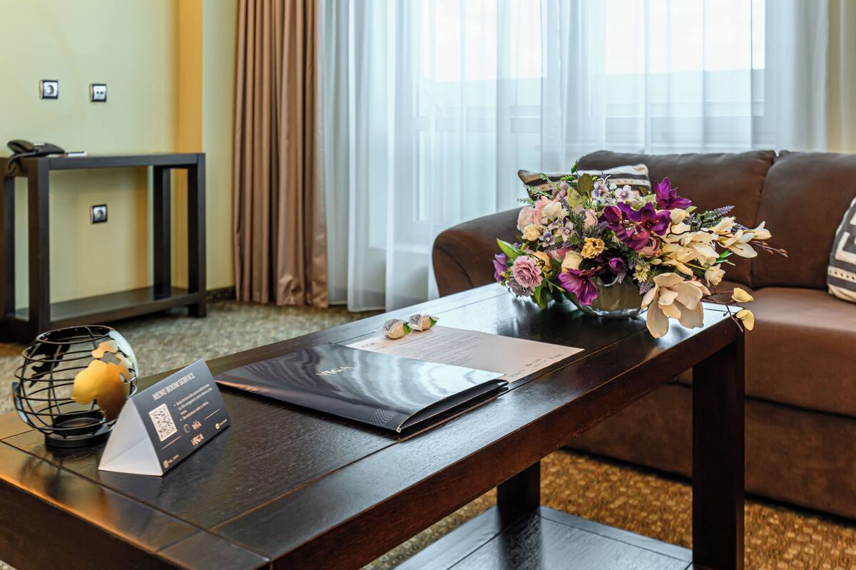 A hotel room with a wooden coffee table, a vase of flowers, a laptop, and a business card holder.