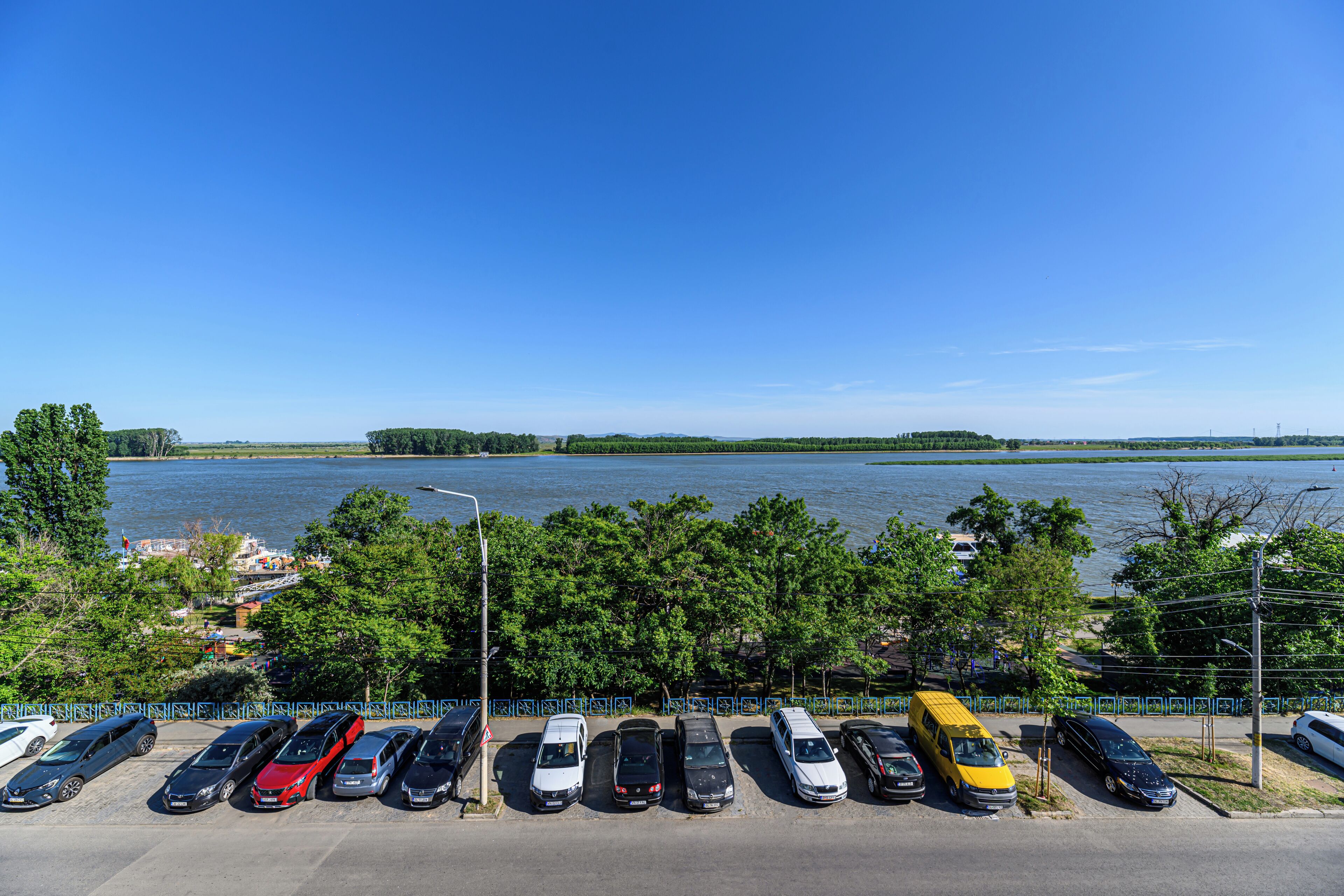 A parking lot with various cars and a yellow bus, overlooking a body of water and greenery.