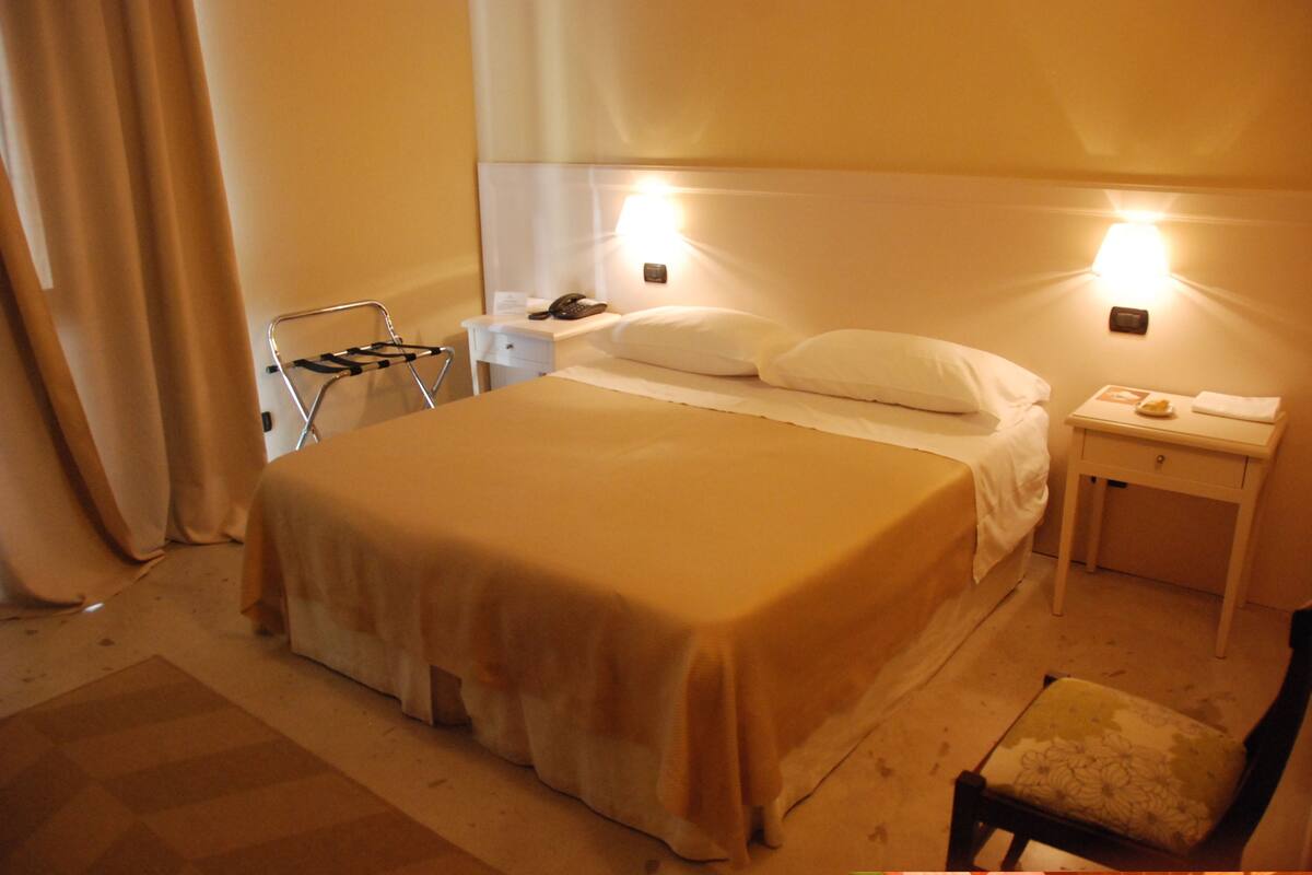 A hotel room with a bed, bedside tables, a chair, and a lamp.