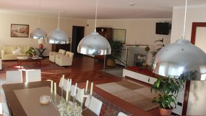A spacious living room with a dining area, featuring a large table set for a meal, multiple hanging pendant lights, and a comfortable seating arrangement.