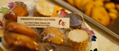 A plate of gluten-free products labeled "PRODOTTI SENZA GLUTINE" with a tray of pastries in the background.
