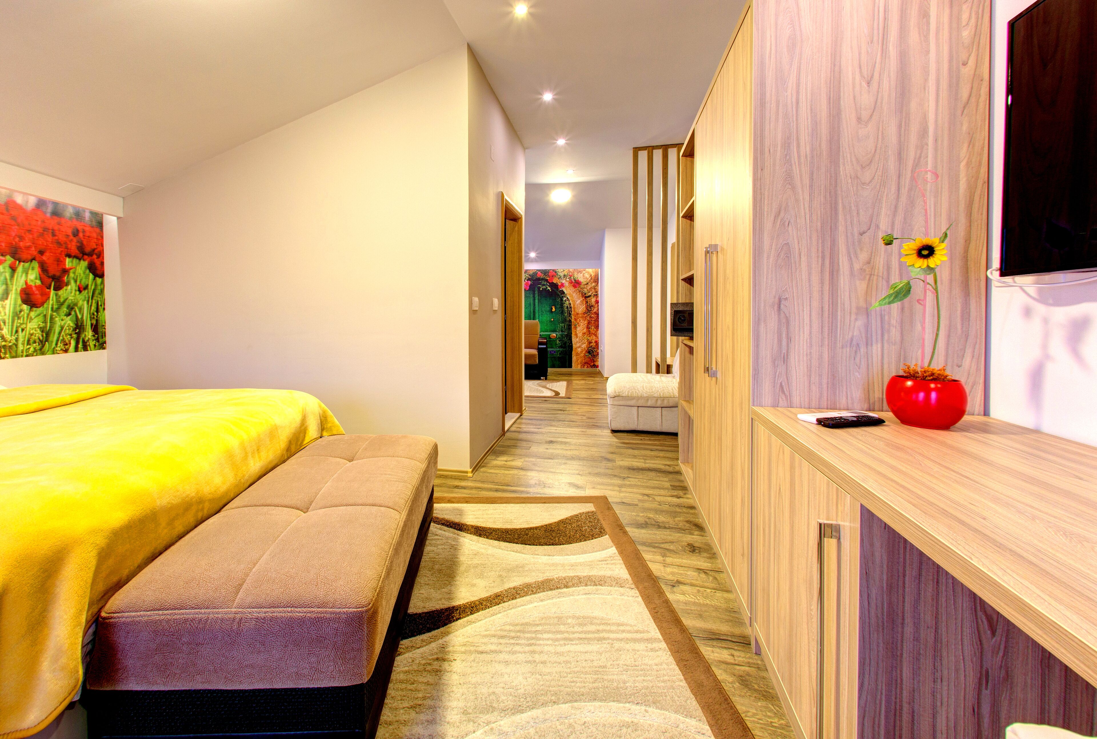 A hotel room with a bed, a bench, a wooden desk, and a painting of flowers on the wall.