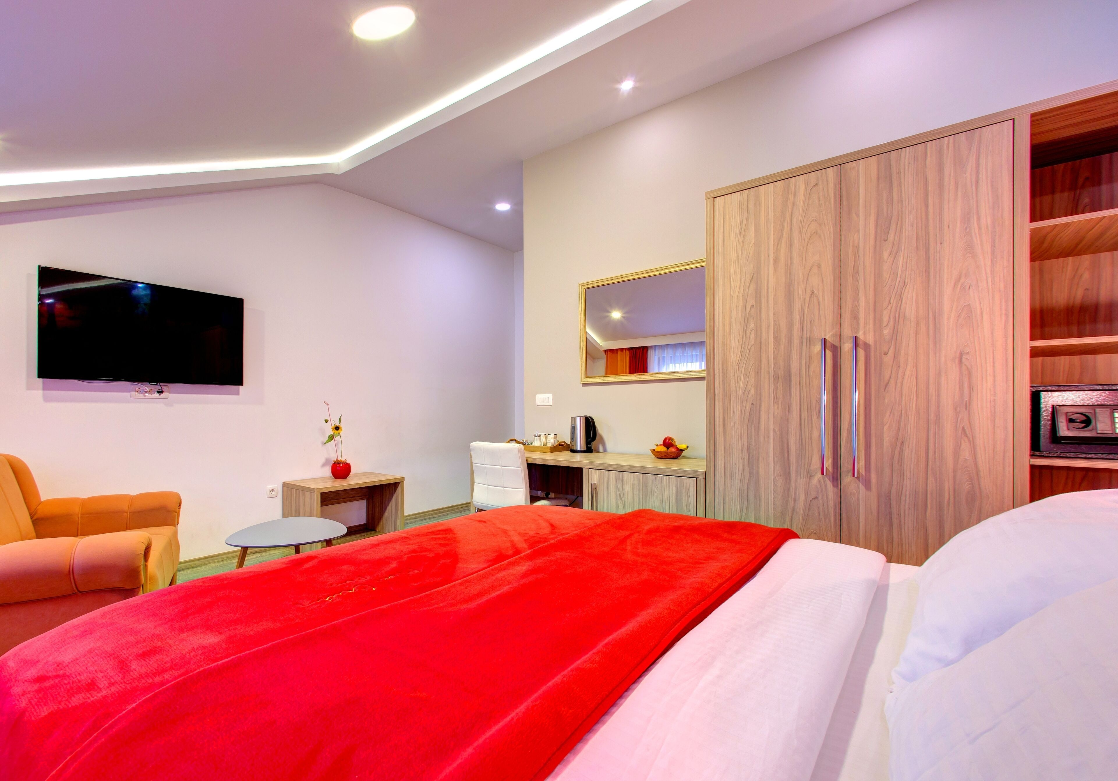 Ein modernes Hotelzimmer mit Bett, Fernseher, Schreibtisch und Kleiderschrank.