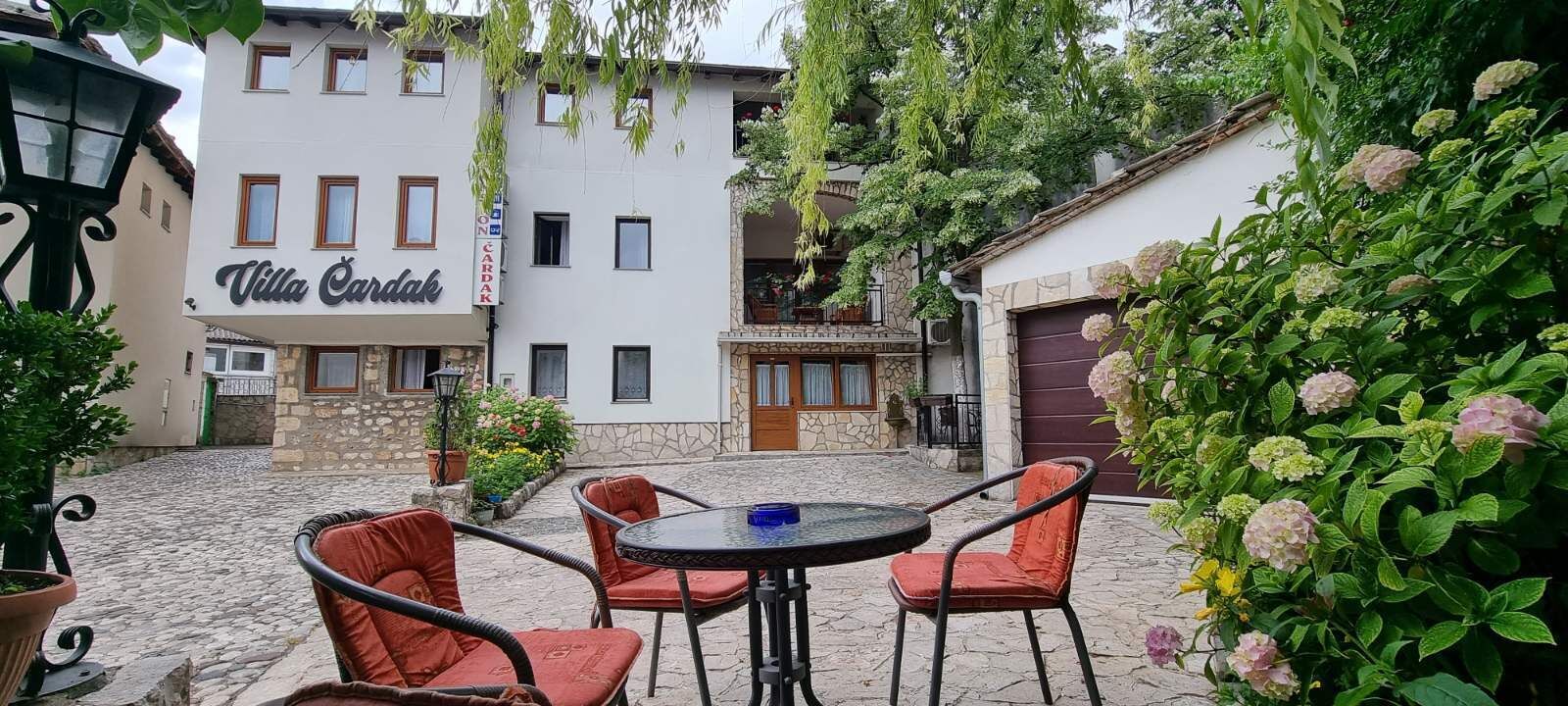 An outdoor seating area with a table and chairs, a building labeled "Villa Cardak," and a stone pathway.