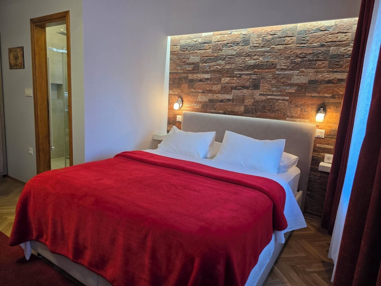 A bedroom with a stone wall, a bed with white bedding, and two wall-mounted lights.