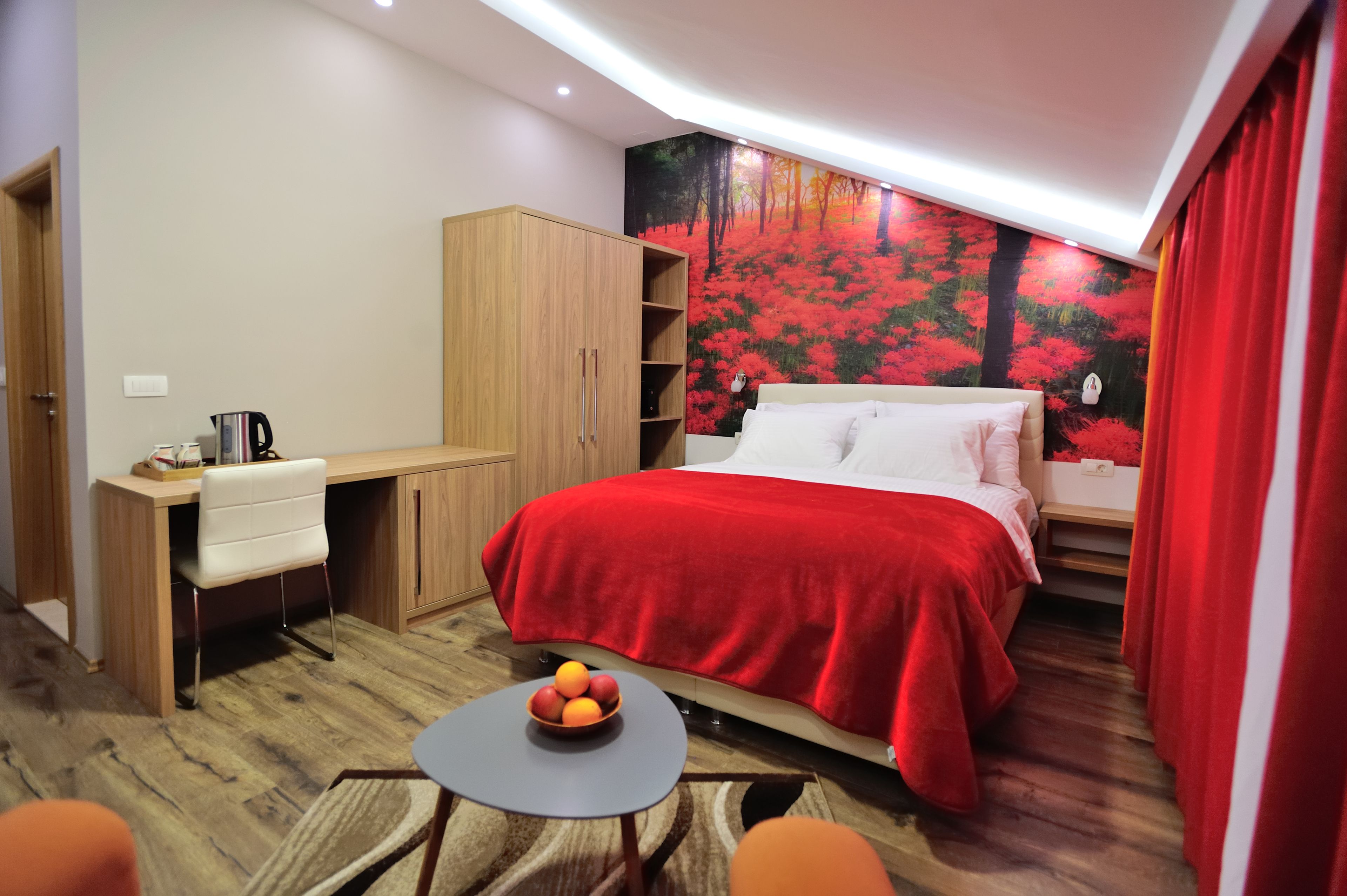 A bedroom with a bed, a desk, a chair, a small table with fruit, and a wardrobe.