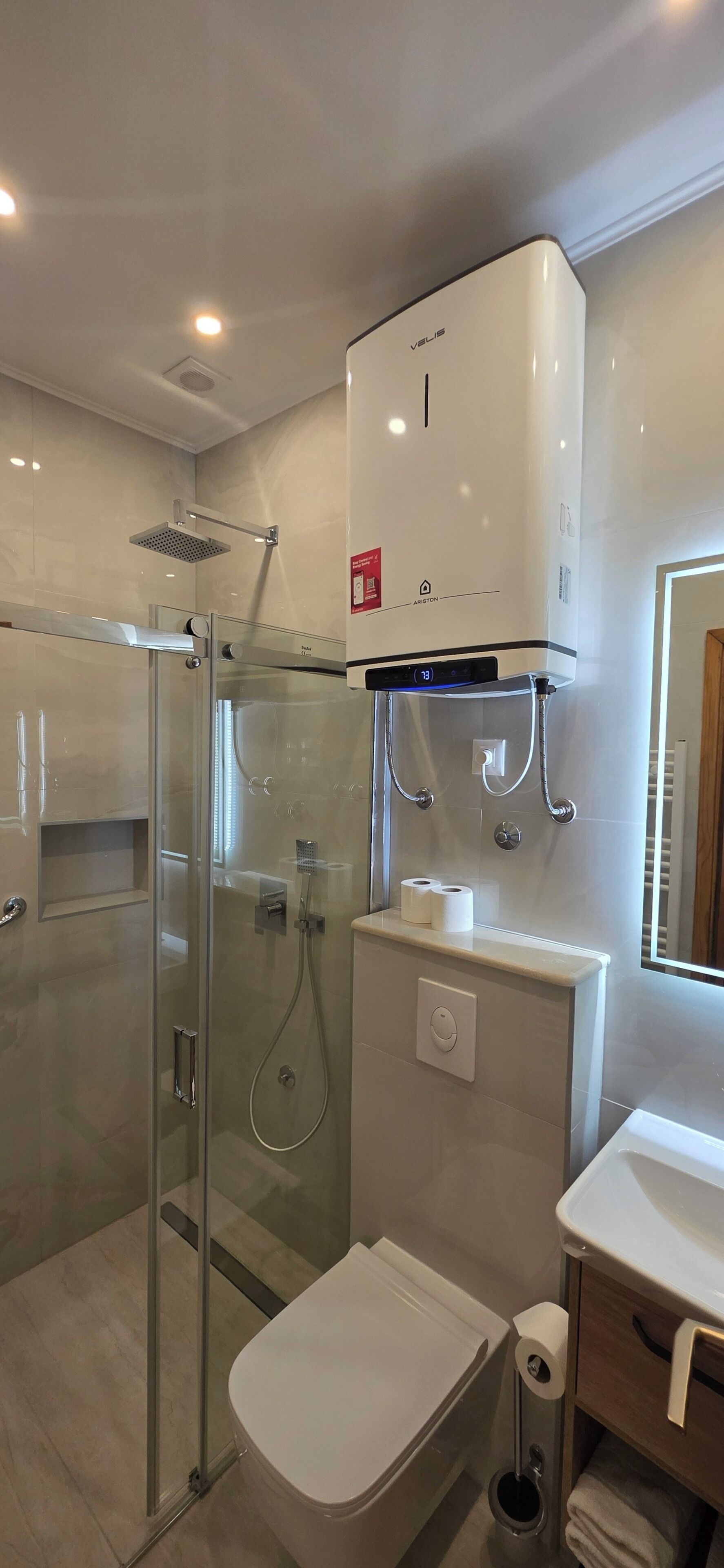 A modern bathroom with a glass-enclosed shower, a toilet, a sink, and a wall-mounted heater.