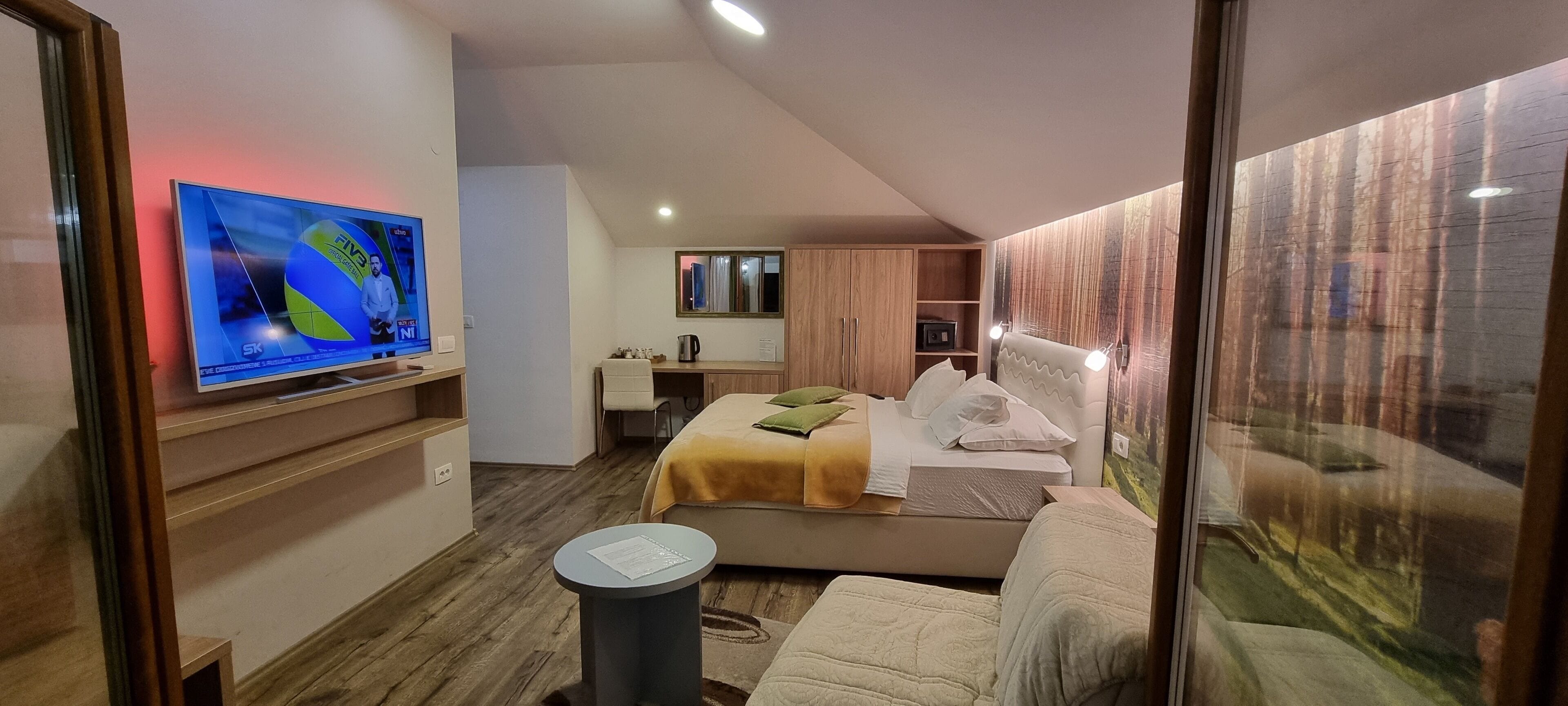 A modern hotel room with a bed, a desk, a chair, and a TV displaying a sports channel.
