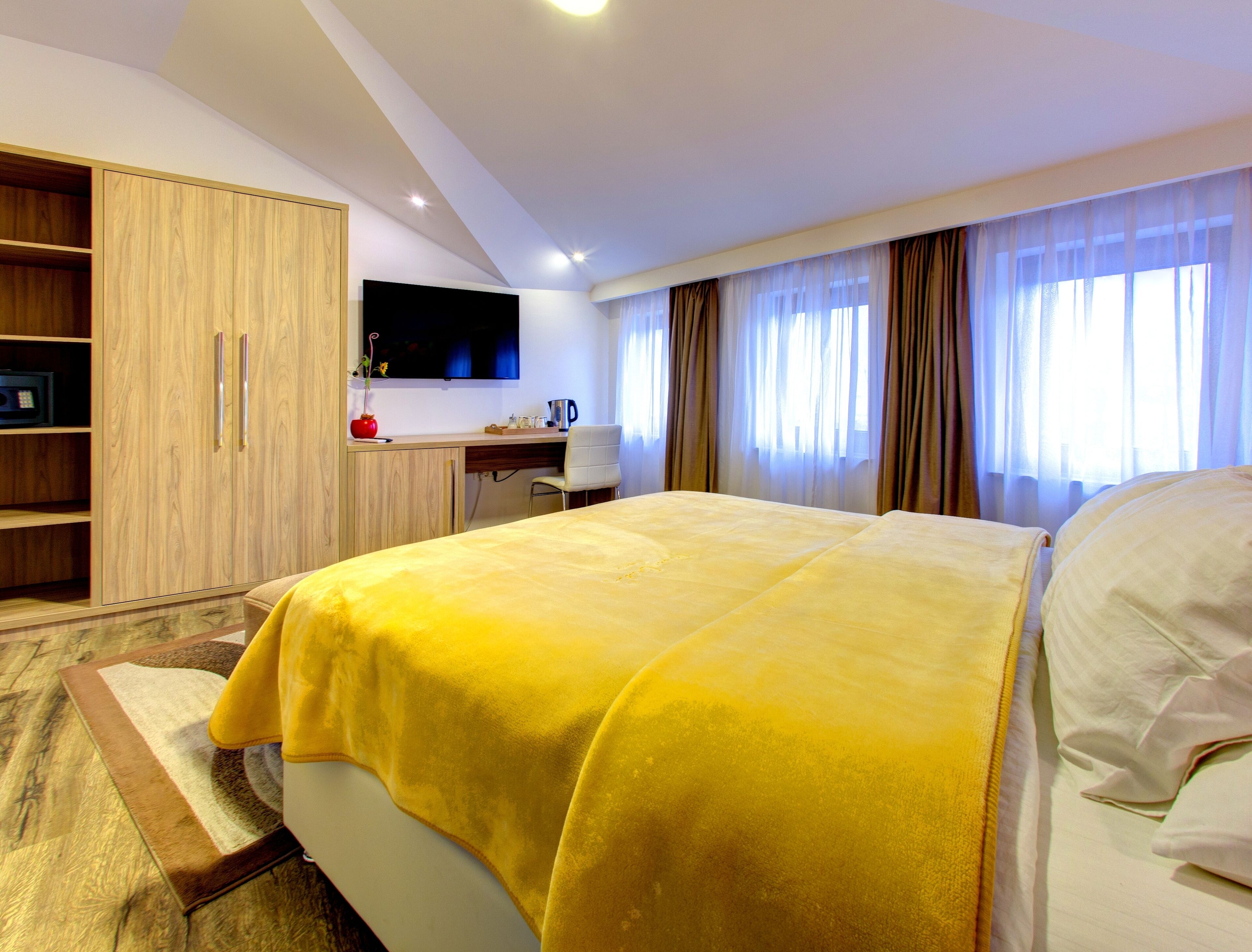 A hotel room with a large bed, a desk with a chair, a television, and a wardrobe.