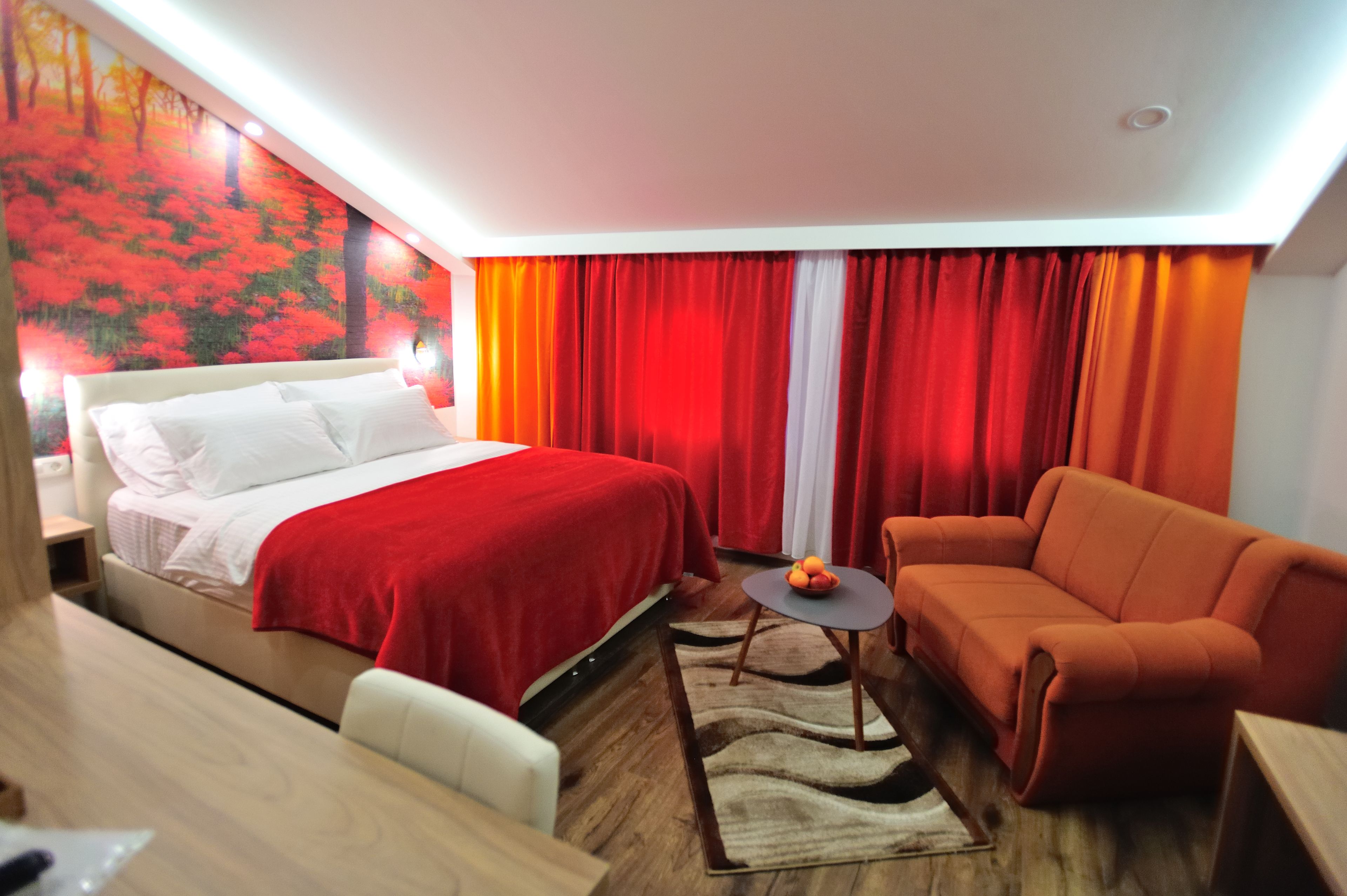 A hotel room with a bed, a sofa, a small table with fruit, and a painting on the wall.