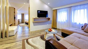 A modern living room with a flat-screen TV mounted on a wooden shelf, a sofa, a coffee table with fruit, and a wooden floor. - Villa Cardak (Mostar)
