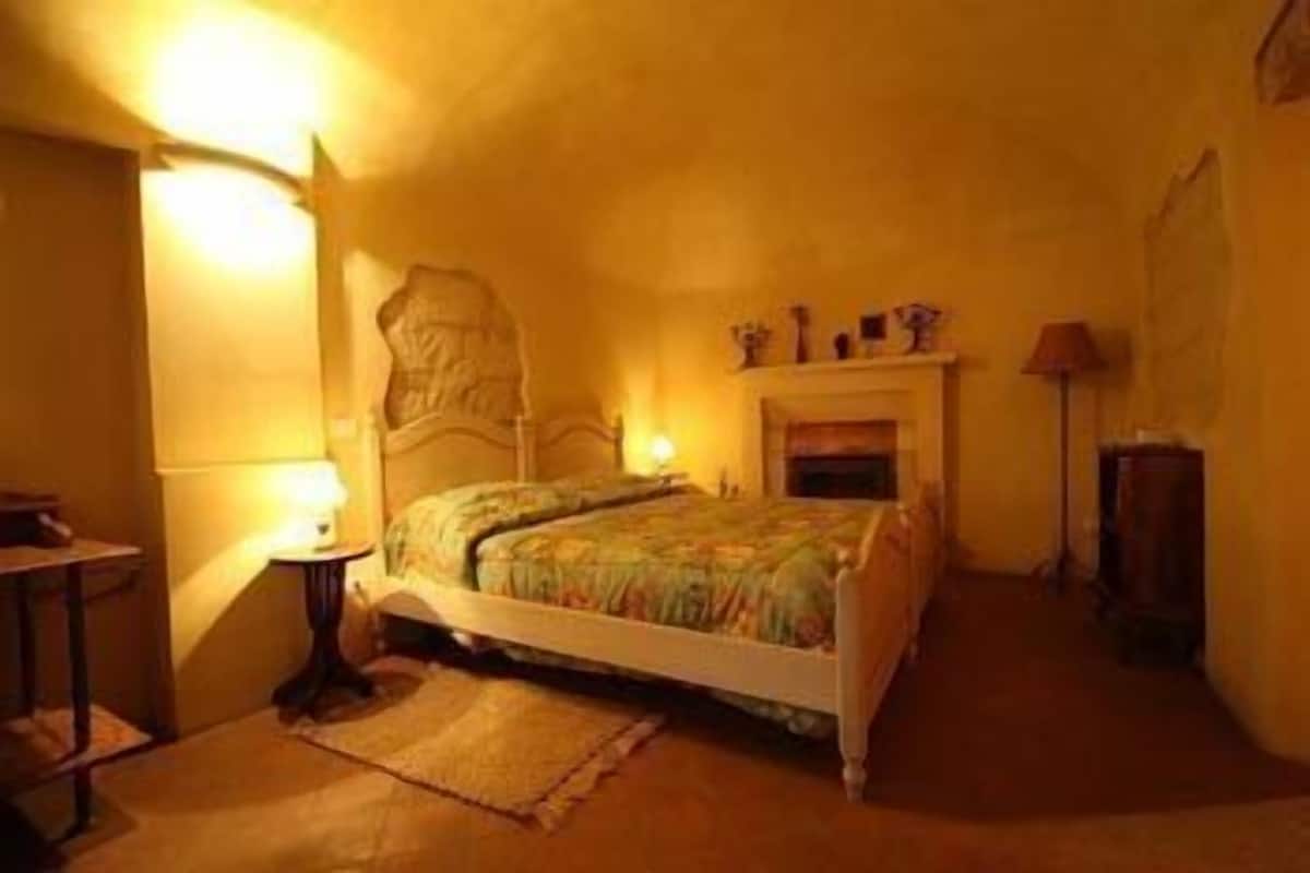 Ein Schlafzimmer mit einem Bett, einem Nachttisch, einer Lampe, einem Kamin und einem Sessel.