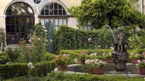 Un jardín con una estatua, setos cuidados y un edificio con ventanas arqueadas.
