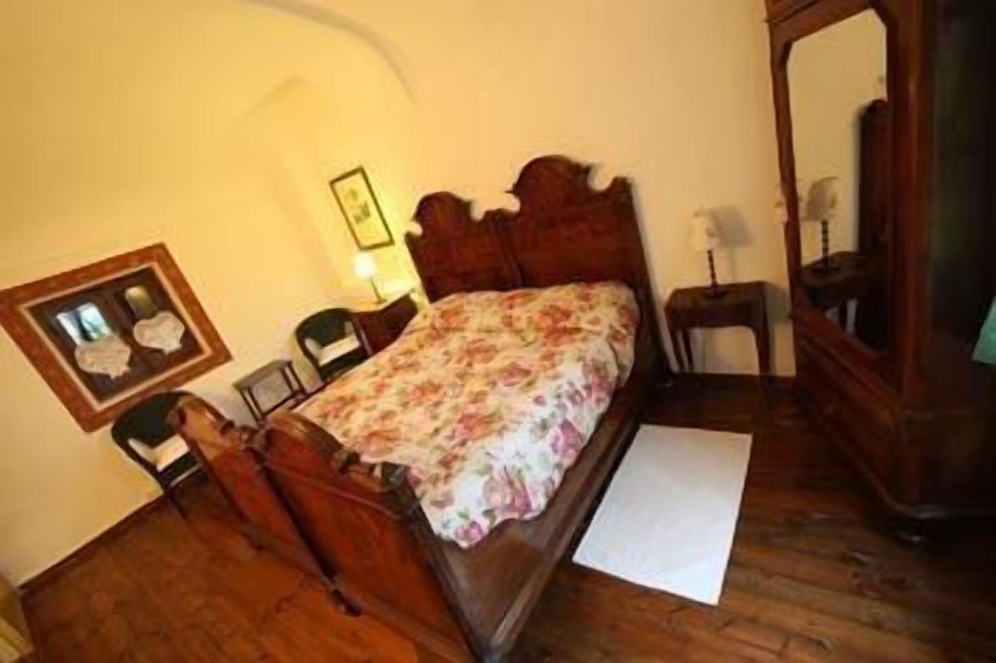 A bedroom with a wooden bed, a nightstand, a chair, a framed picture, and a mirror.