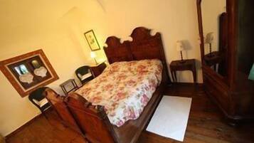A bedroom with a wooden bed, a nightstand, a chair, a framed picture, and a mirror.