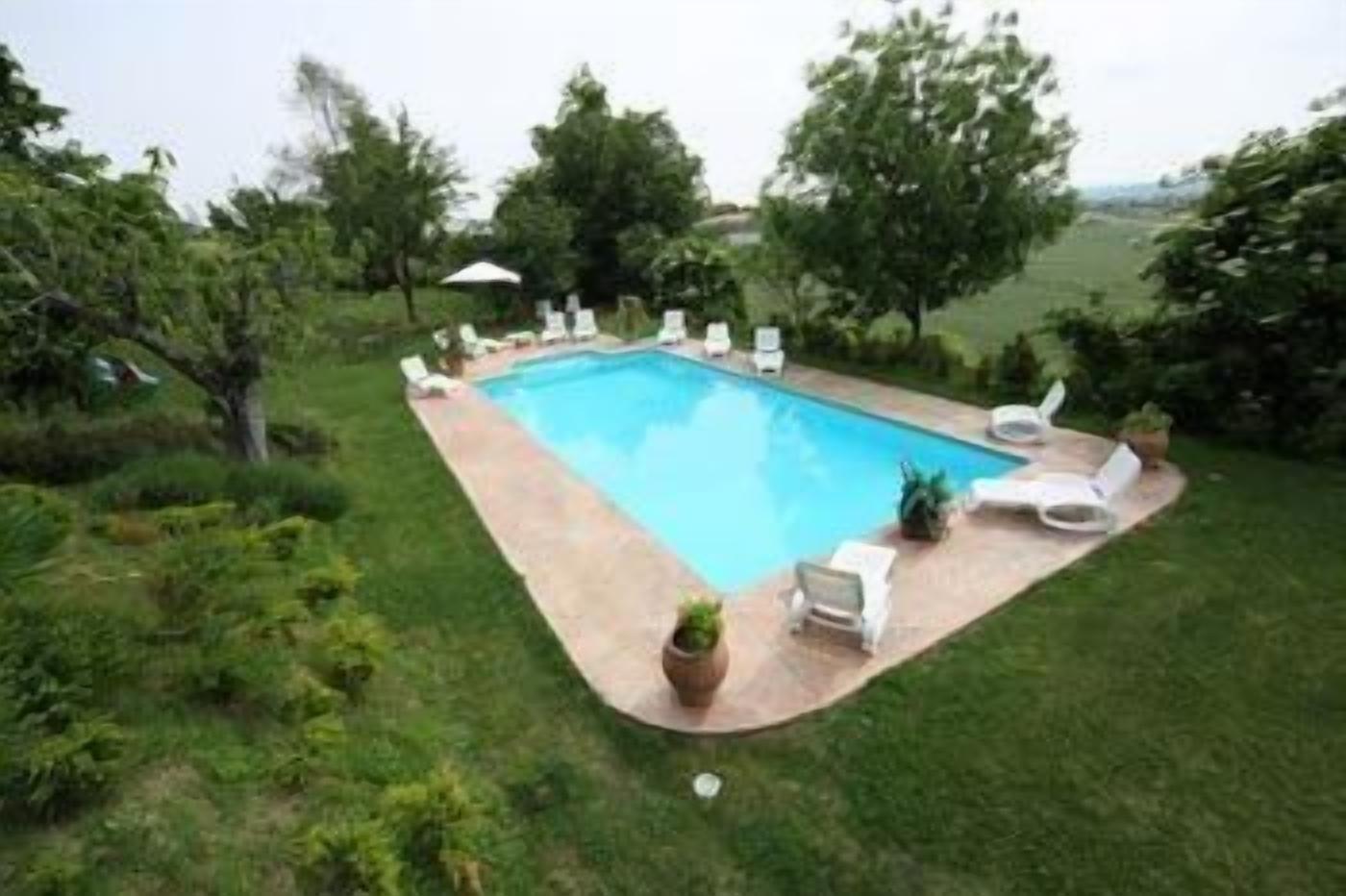 Une piscine rectangulaire bordée d’une terrasse carrelée, entourée de chaises longues blanches et de quelques plantes en pot.
