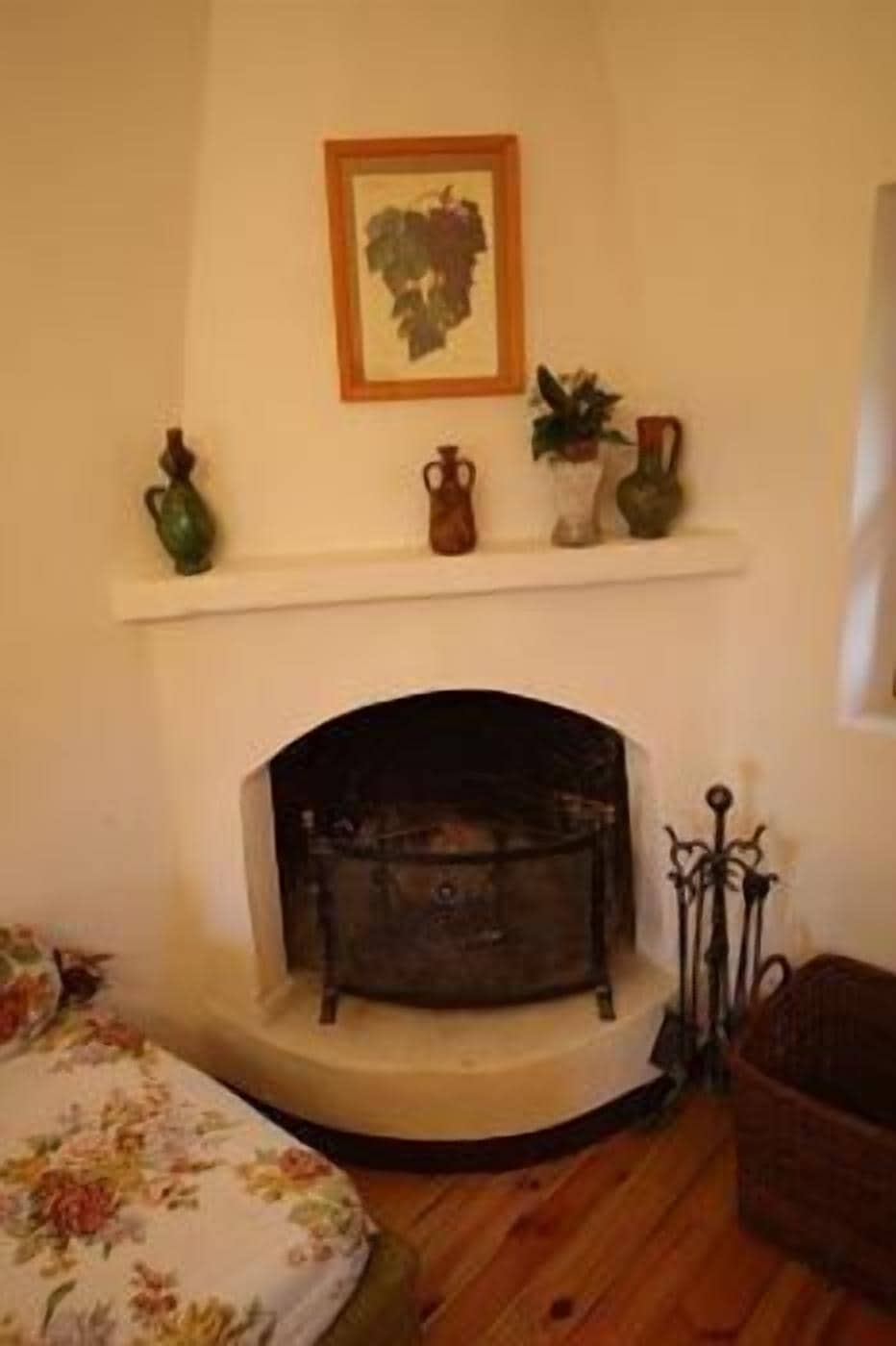 Une pièce avec une cheminée, une étagère ornée d’objets décoratifs et une couvre-lit à motifs floraux.