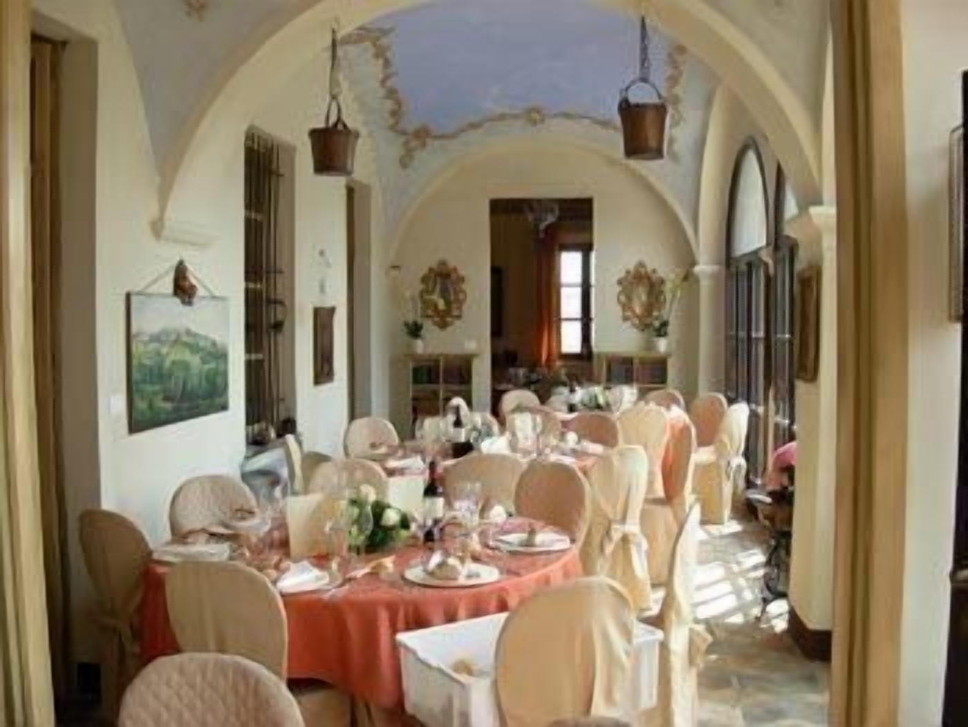 A dining area with round tables set for a meal, featuring white chairs and a red tablecloth.