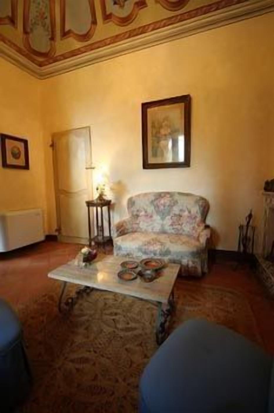 Una sala de estar con un sofá floral, una mesa de centro con objetos decorativos, un cuadro en la pared y un radiador.