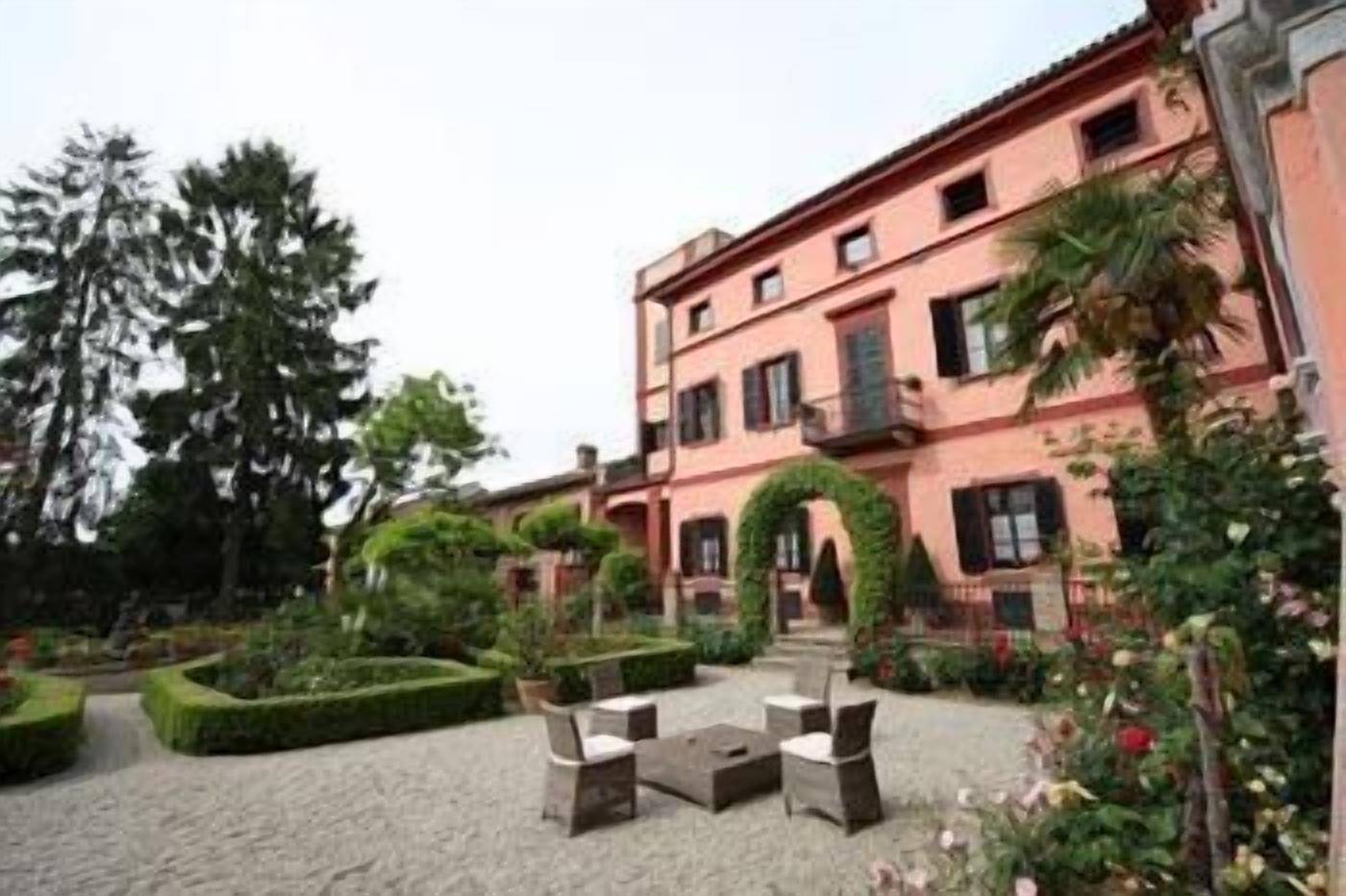 A building with a pink facade, a courtyard with a seating area, and a well-maintained garden.