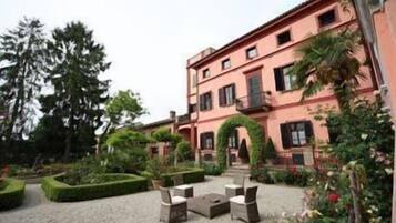 A building with a pink facade, a courtyard with a seating area, and a well-maintained garden.