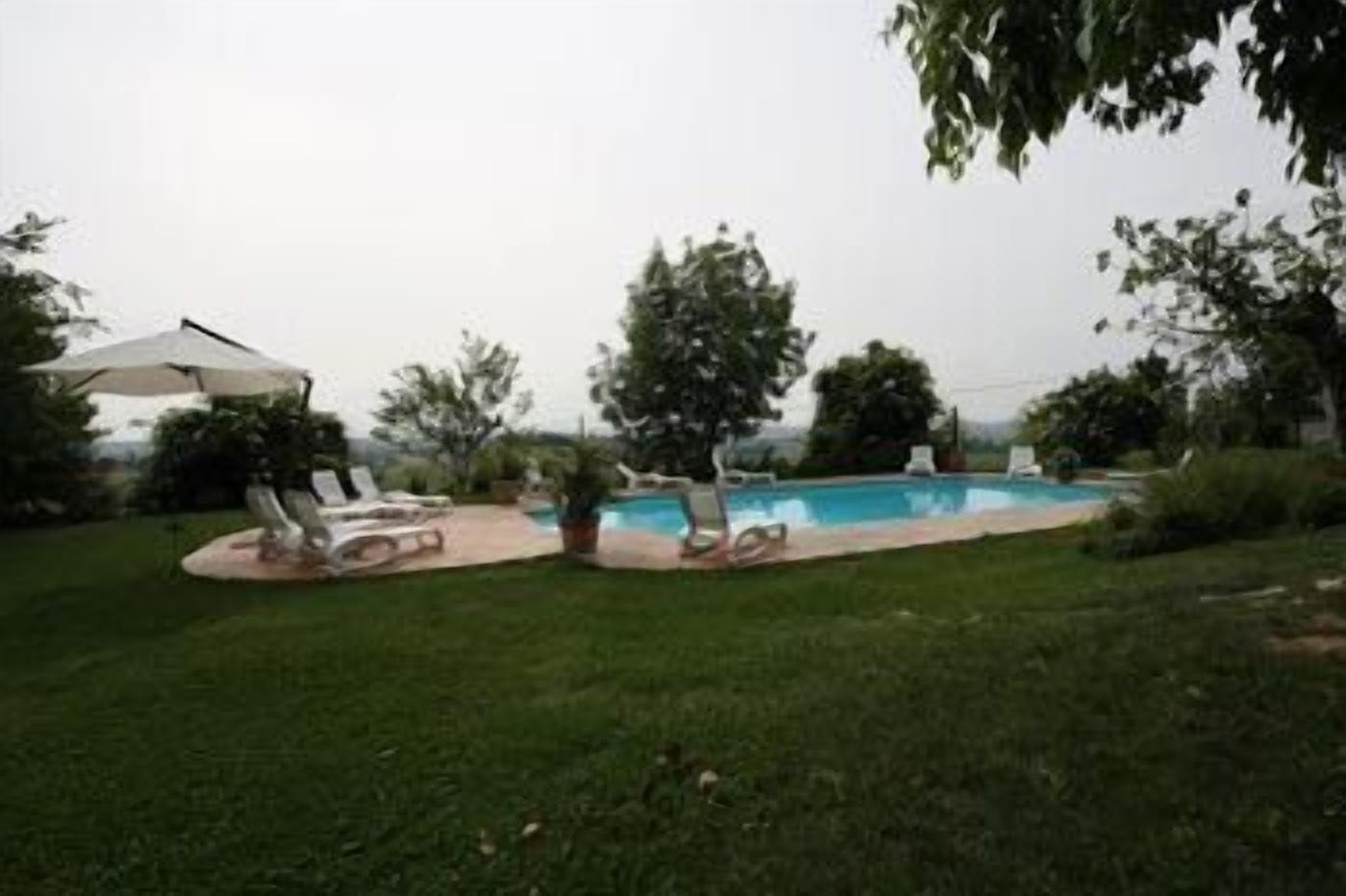 A backyard with a swimming pool, lounge chairs, and a patio umbrella.