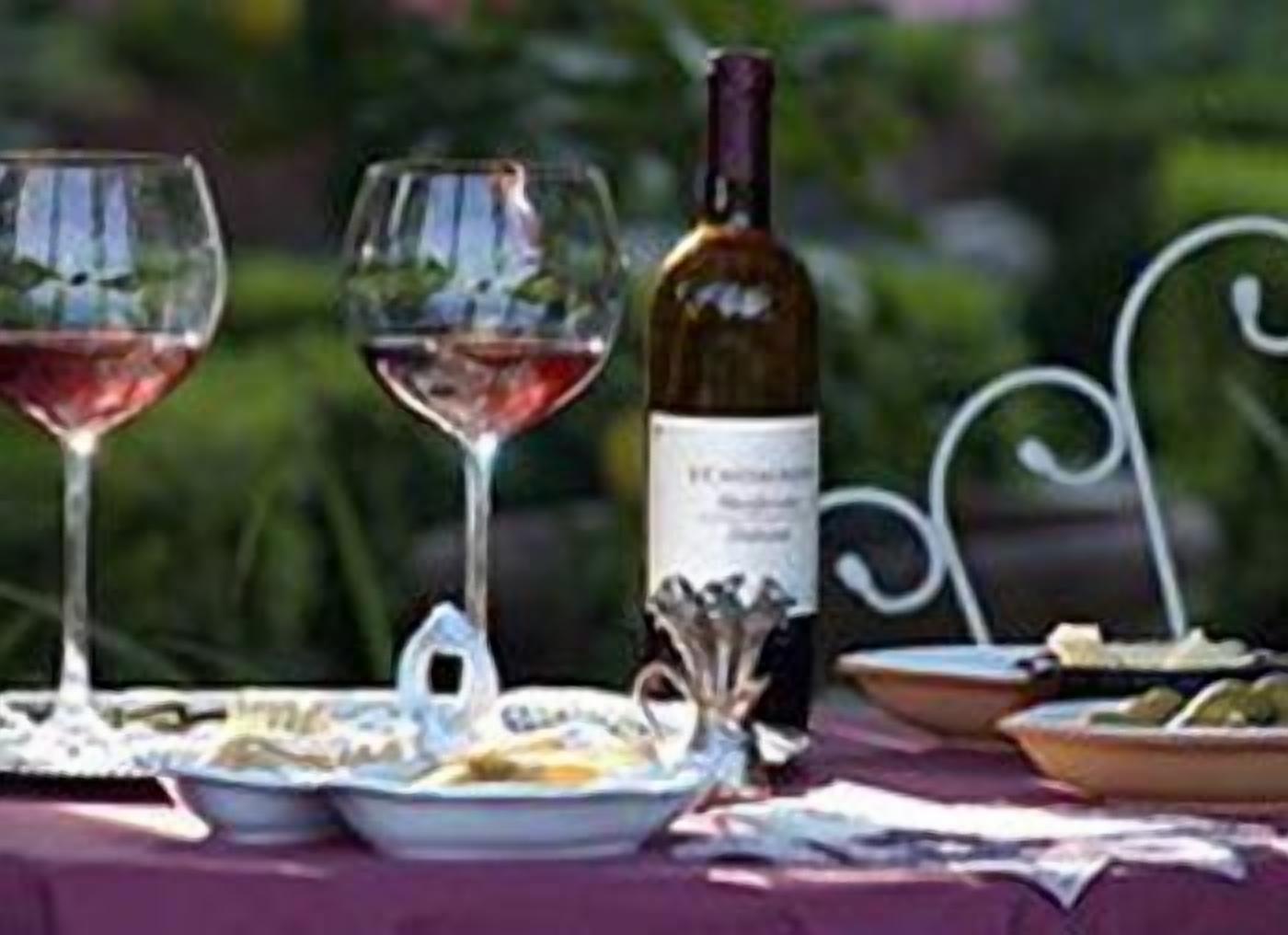 Una mesa servida con copas de vino, una botella y platos de comida.