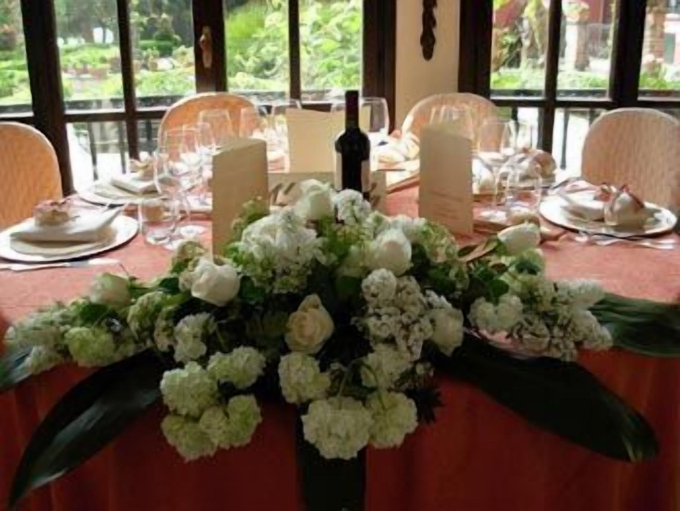 Mesa de jantar posta para quatro pessoas, com flores brancas no centro, rodeada por cadeiras.