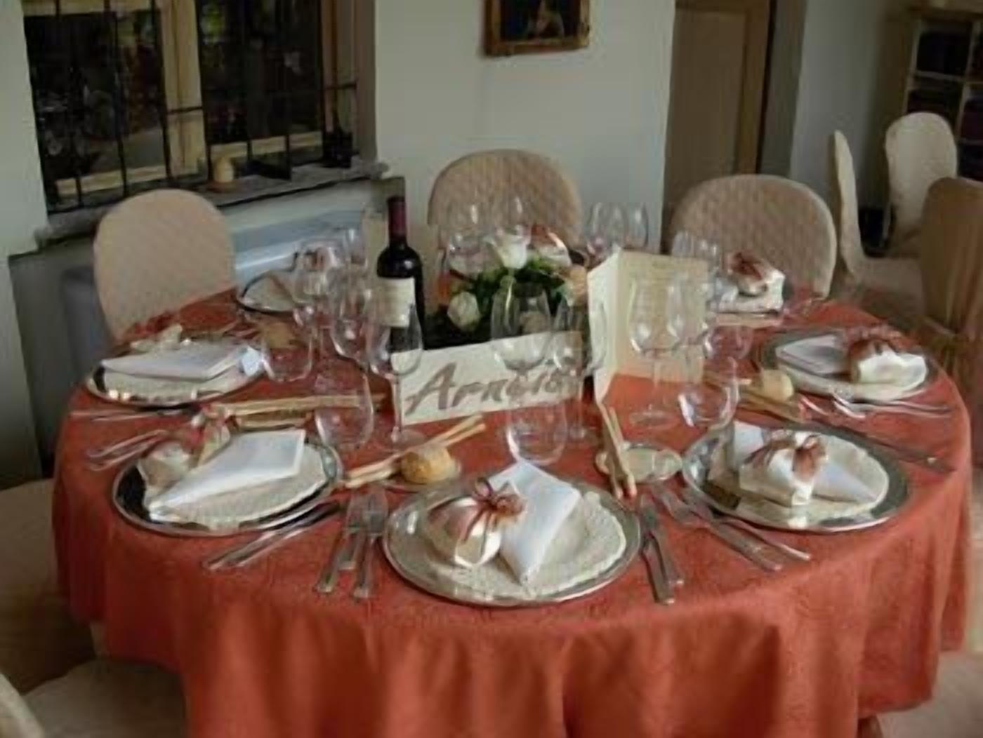 Mesa de jantar redonda posta com pratos, copos e talheres, coberta por uma toalha vermelha.