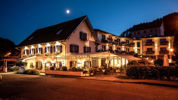 Un hotel con una zona de estar exterior cubierta, varios balcones y una fachada bien iluminada.