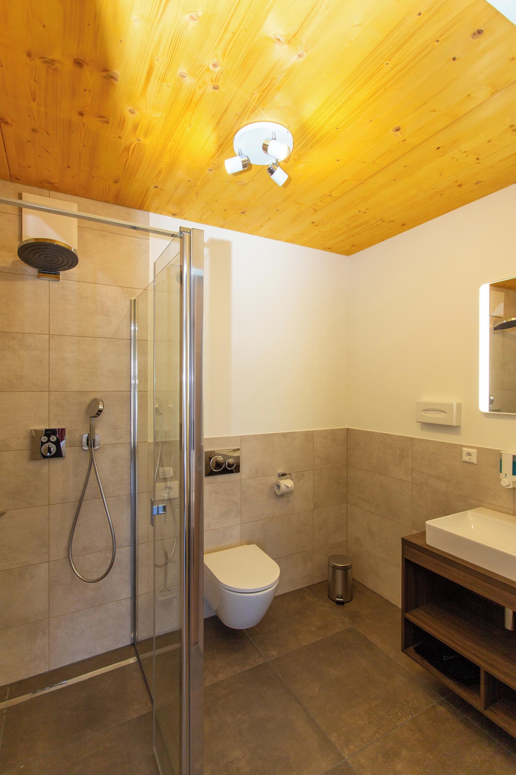 Un baño moderno con cabina de ducha de vidrio, inodoro y lavabo con mueble de madera.