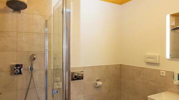 Un baño moderno con cabina de ducha de vidrio, inodoro y lavabo con mueble de madera.