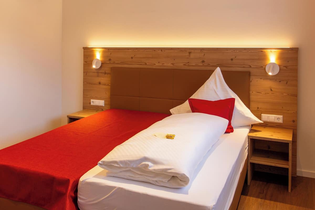 A neatly made bed with a red blanket and white linens, wooden headboard, and bedside lamps.