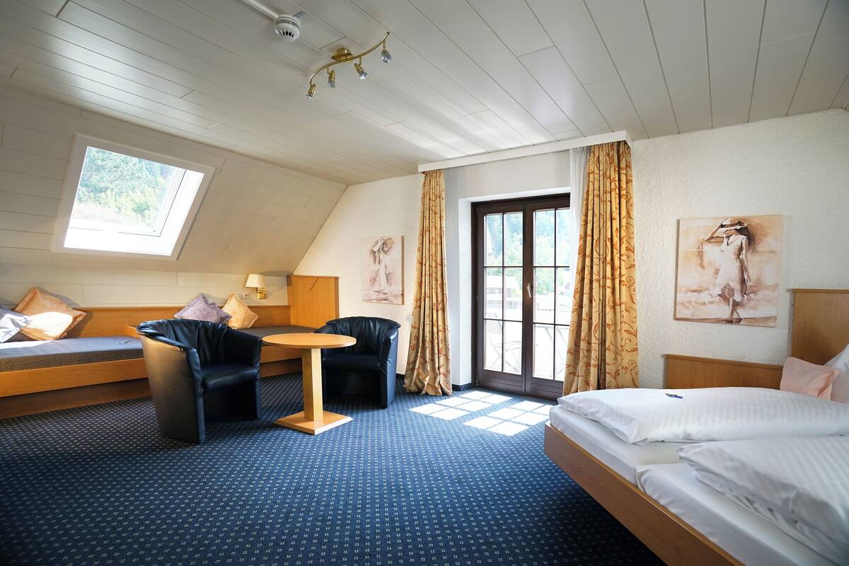 A hotel room with a bed, a sofa, a chair, a small table, and a window with curtains.